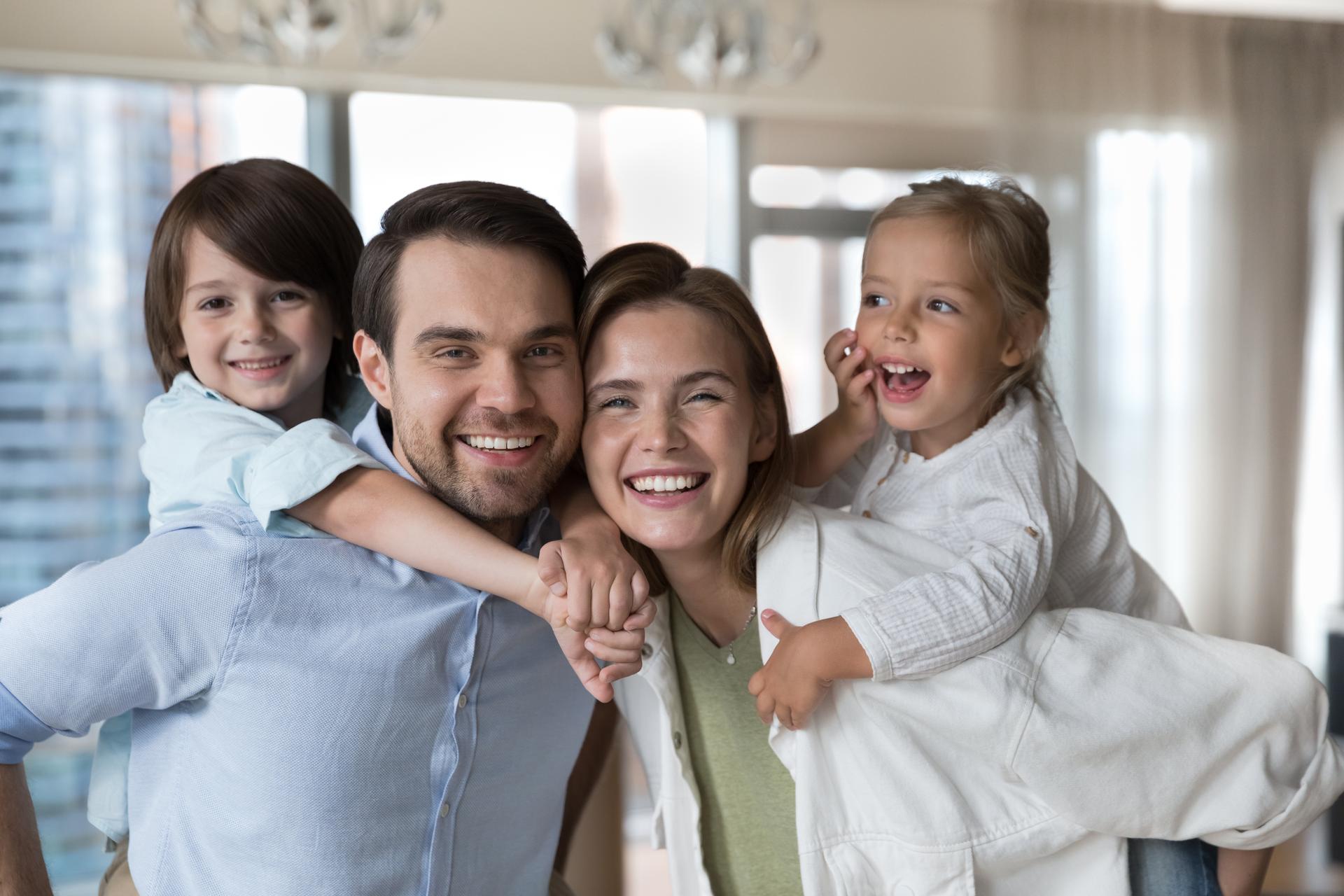 Cheerful young parents piggy backing little kids, holding children