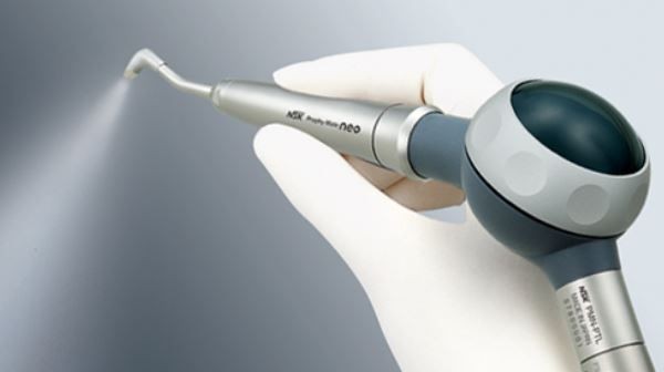 Hand in glove holding a dental air polishing tool spraying fine mist.